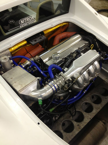 Detuning a mapped setup - Page 1 - Engines & Drivetrain - PistonHeads - This image provides an overhead view inside the engine bay of a white vehicle, showcasing a complex arrangement of mechanical components. The engine is white, compact, and silver, with a prominent license plate on top. Blue and silver plumbing lines run throughout the compartment, indicating a well-organized and aesthetically pleasing design. Gleaming in the light, the shiny surfaces of the engine components reflect the high-quality craftsmanship of this custom engine setup.