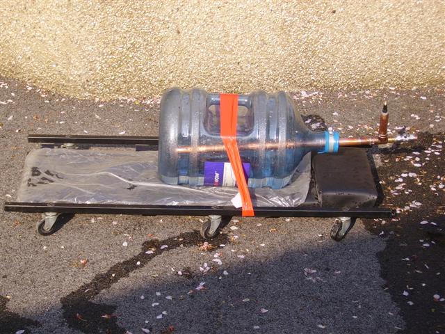 A pair of shoes sitting on top of a skateboard - Pistonheads - In the image, a large plastic jug with a blue cap is at the center of attention, seemingly overflowing. This jug appears to be tightly sealed with red tape and is also attached to a copper piping. Underneath the jug, there's a black platform or tray marked with wheels, suggesting it might be en route to another location or it's ready for transport. The backdrop is quite sandy, indicating that the scene might be outdoors or on a granular surface. A few scattered cherry blossom petals add a touch of natural beauty to the otherwise industrial setup.