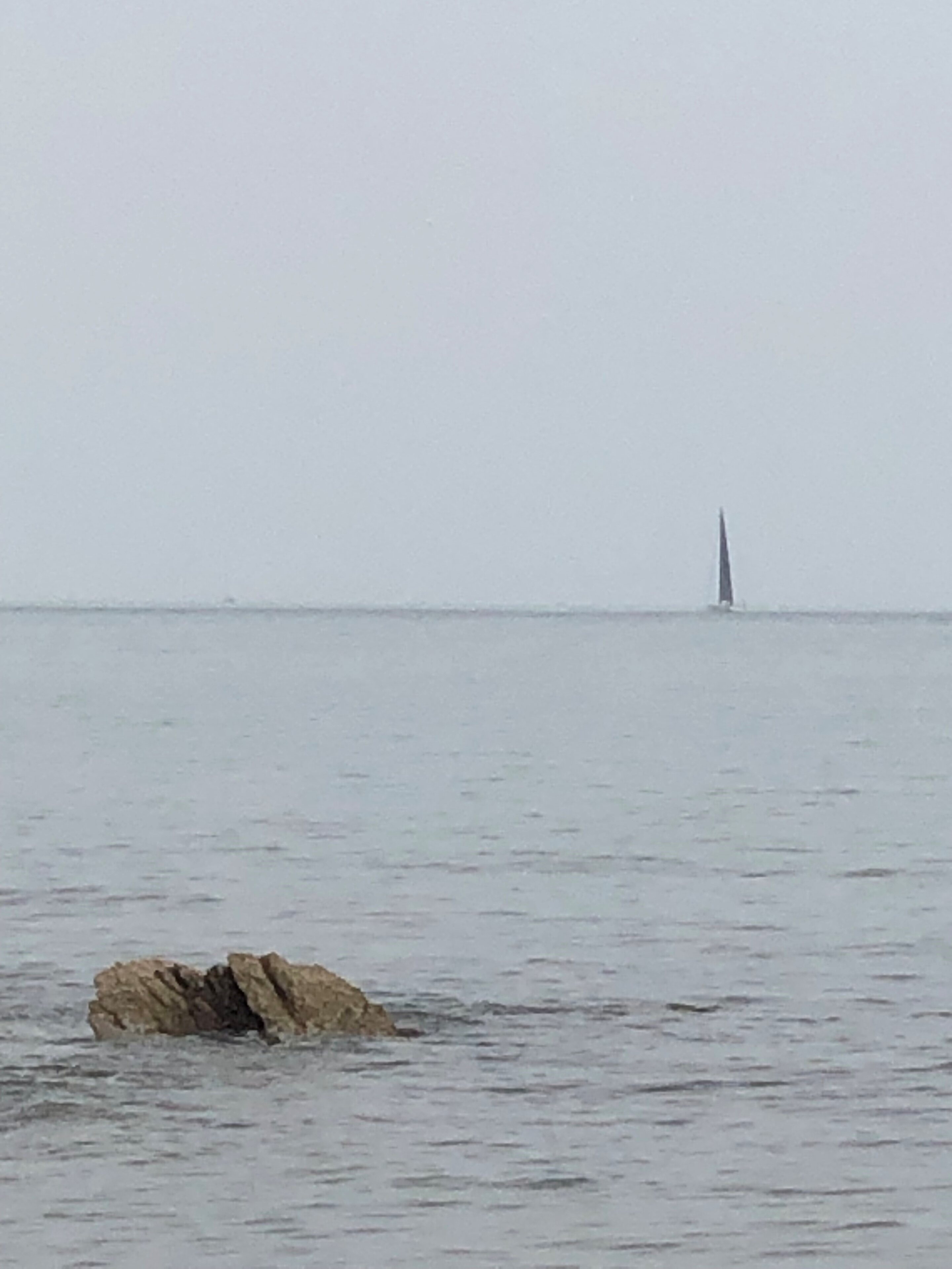 A boat floating on top of a body of water - Pistonheads - The image shows a rock formation protruding from the ocean. The rock is brown and appears to be in good condition, without visible erosion or damage. In the background, beyond the water, there's a lone ship at sea. The sky overhead seems overcast, suggesting it might be a cool or cloudy day. There are no people or other objects immediately around the rock, which stands out prominently in the image.