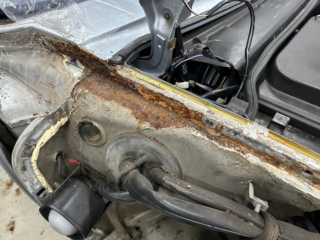 Pistonheads - The image shows a close-up view of the front end of a vehicle, likely in a workshop or repair facility. There's visible rust and damage on the metal components, indicating corrosion and wear. A significant amount of dirt and debris is visible around the damaged areas. The vehicle appears to be an SUV or truck, given the size and shape of the front bumper. In the foreground, there are tools scattered across the work area, suggesting ongoing repairs or maintenance. The image has a watermark-like texture over the entire frame, which may be intended to protect the original image from unauthorized use.