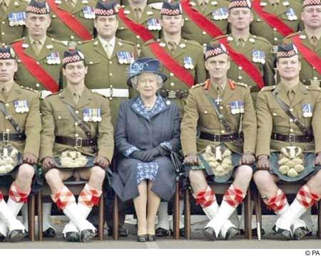 Have you ever worn a kilt? - Page 5 - The Lounge - PistonHeads - This is a color photograph showing a group of military personnel, wearing their ceremonial uniforms, flanking a woman on a chair. The military personnel are dressed in kilts with red medallions, light brown jackets, blue and red crossbands, and bearskin caps. The woman in the center is wearing a royal blue coat with a light blue hat and is likely a member of the British Royal Family judge by the uniform of the guards and the decorations around the group. She appears to be a Queen or a member of a higher rank, as indicated by her attire and the presence of a guardsman directly behind her. The image might have been taken at a formal event, such as a state visit or a military parade due to the uniforms and the composition of the group.