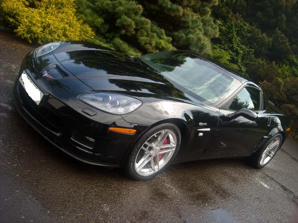 Clean Pistonheads Properly - The image showcases a revamped sports car parked on a wet road. The car, with its sleek black color, has distinctively shiny silver rims that contrast with the body color. Its design features a large air intake on the front, and it also sports a smaller air intake near the side door. The high-rise headlights enhance the aggressive look of the vehicle. The car appears to be a notable luxury model, possibly a Lamborghini, parked during the day with surrounding greenery.