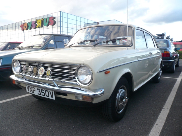 Metrocentre Pistonheads - This image features a vintage beige Toyota Corolla parked in a parking lot. The car stands out with its round headlights and a rectangular taillight design. The car is adorned with badges on the front, instantly recognizable as a Volvo brand based on their shield logo emblematic on the grille. A license plate is prominently visible, reading "VNP 350V". On the left side of the photo, there's a sign that reads "TOYS R US", indicating a department store or toy store nearby. In the background, there are several other cars parked, creating a bustling backdrop to the main focus of the image.