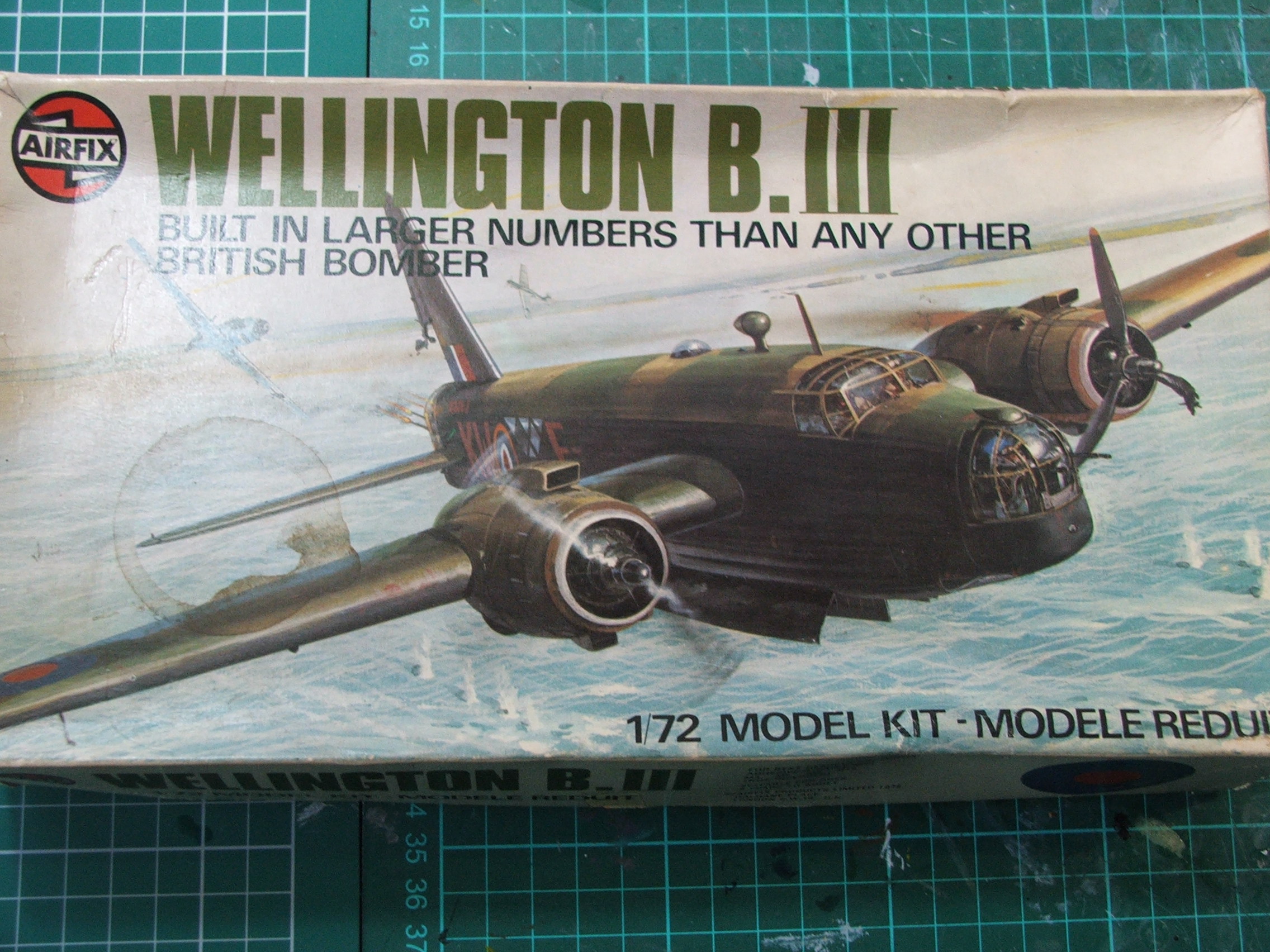 Airfix Vickers Wellington III - Page 1 - Scale Models - PistonHeads - The image displays a model airplane kit labeled "Welllington B.III." This model kit is designed to depict a British bomber aircraft. The model represents an aircraft with the number "172" visible on its top wing. The photograph also shows a red and white striped box edge with lettering and numbers, suggesting the box is intended for keeping the model kit in. The style of the image is a flat, angled photograph with the model airplane as the central focus.