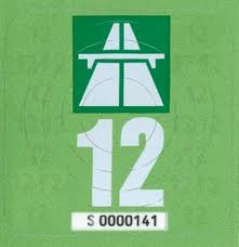 A red and white sign on a pole - Pistonheads - The image shows a green and white background with two distinct elements: one being a stylized illustration of a highway directional sign, indicative of a number 12 lane marker, and the other is a large white number 12. The layout of the numbers appears to have a deliberate sequence of twelves and a representation of a multi-lane road.