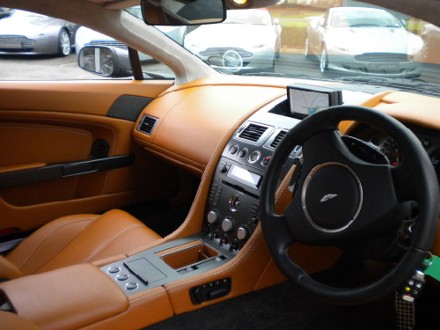 Kestrel Interior Pistonheads - The image depicts the interior of a car, with a focus on the orange leather seats and the black steering wheel, which is adorned with a silver emblem. The instrument cluster is visible, displaying information about the vehicle. Outside the car, there is a reflection on the glass, which appears to be of other vehicles, indicating that the car is parked in a location with multiple vehicles. The driver's side window and the center console are also visible, contributing to the overall details of the car's interior. The car seems to be stationary, with the doors closed and the exterior not offering any additional context beyond what is visible through the windows.