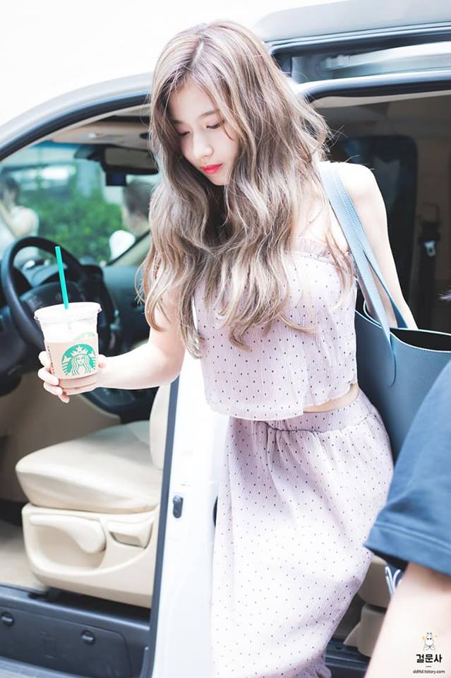 A woman is talking on her cell phone - In the image, a woman is standing in the doorway of a car, her hand gently resting on the open door. She's casually dressed in a pink and white dress, with a purse slung over her shoulder. In her hand, she holds a Starbucks coffee cup, perhaps preparing to start her day. The car door is open, and the interior of the vehicle is visible, suggesting perhaps a goodbye or preparation for departure. The woman appears calm and composed, adding a serene quality to the scene.