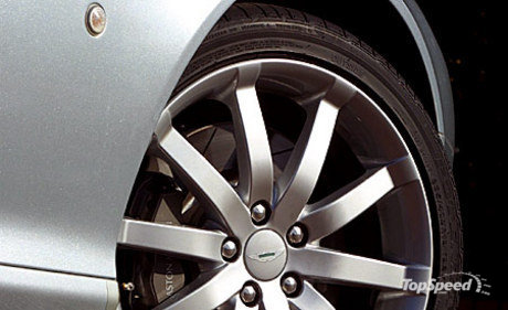 Prices Options Pistonheads - The image focuses on the front wheel of a car. The car is a grey sedan model, which appears to be a front wheel drive. The front wheel is angled towards the right side of the frame, and it includes a silver hubcap with a design that includes multiple spokes. The tire is black and has a visible brand name on the sidewall. The car's machined metal surfaces are clearly visible, reflecting the presence of an alloy wheel. The rim of the wheel also has a small crest in the middle. The image is very clear, with high detail, and it is likely meant to showcase the car's wheel design and the vehicle's alloy wheel.