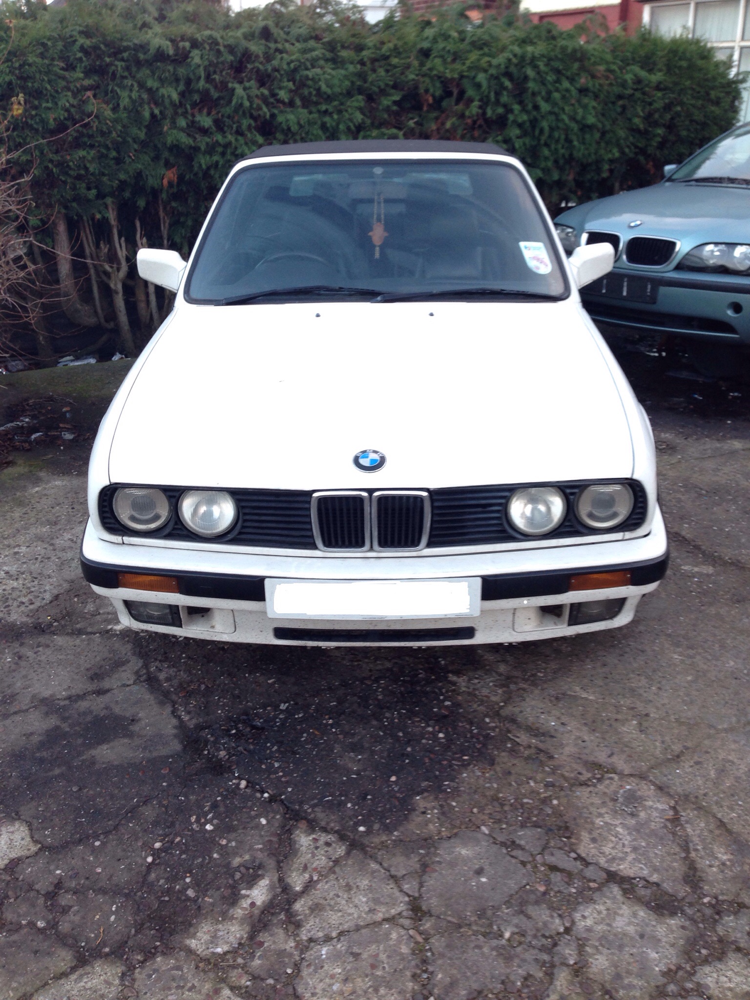 Show us your FRONT END! - Page 117 - Readers' Cars - PistonHeads - The image shows a white two-door BMW car parked in a lot. The vehicle is positioned at an angle, allowing a clear view of the front and side profile. The car features the distinctive BMW kidney grille and round headlights. There's some water on the ground indicating recent rain. A blue car is also visible in the background, suggesting the car is in a public parking area. The lighting in the photo is bright and the shadows are visible, suggesting it might be a sunny day.