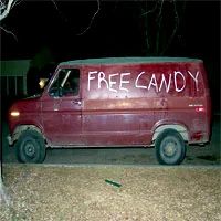 The image shows a van parked in a residential area at night. The van is prominently marked with the phrase "FREE CANDY" written on its side, and the word "FREEDOM" is also visible, possibly indicating that it's from a different country. The back window of the van features a sticker with the same text as the words on the side: "FREE CANDY." There is no sign of any candy inside the vehicle.