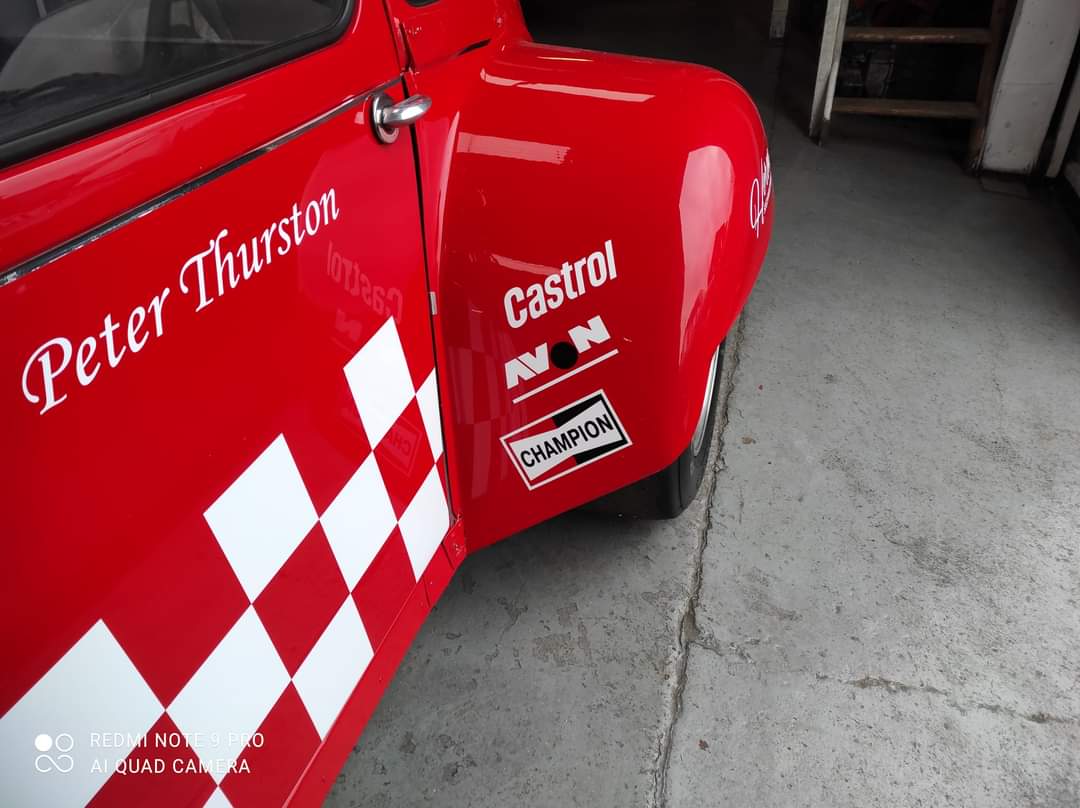 Pistonheads - The image shows a red vintage race car parked indoors. On the side of the car, there's text that includes the name "Peter Thurston," along with sponsor names such as Castrol and Autocar. The car is adorned with checkered flags, which are commonly associated with motorsports. In the background, there appears to be a person partially visible.