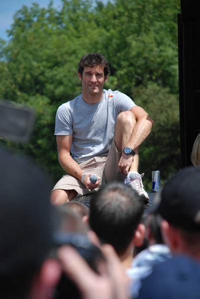 Goodwood Pistonheads - The image captures a lively scene, possibly at a sporting event or street festival. A man is the main focus. He is comfortably seated on a crowd barrier, relaxed and absorbed in the event around him. He is casually dressed in a t-shirt and shorts. His feet rest on the barrier, indicating a sense of ease and familiarity with the environment.

An energetic crowd fills the rest of the image, close to the man. Their attention is focused on something happening outside the frame, unfolding in the distance. The crowd, while not directly interactive with the man, contributes to the overall ambiance of the scene. 

Behind the crowd, trees can be seen, suggesting an outdoor setting. The positioning of the man and the crowd, along with the trees in the background, creates a balanced composition. The man, the crowd, and the trees all contribute to creating a snapshot of an engaging outdoor event.