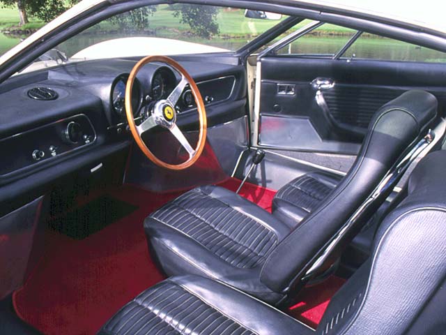 A close up of a car parked on a street - Pistonheads - The image showcases the interior of an exotic sports car, viewed from the rear seat looking towards the front. The dash, a mix of black and white, houses a steering wheel with Ferrari's iconic logo in the center. Premium and sporty, the interior is accented with a red carpet, contrasting beautifully with the black leather seats. The interior of the car is sleek and modern, with the cup holder reflecting the attention to detail in the vehicle's design.