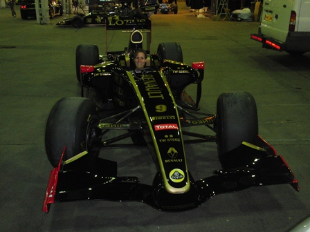 Donington Lotus Festival 13/14 August - Page 1 - General Lotus Stuff - PistonHeads - The image captures a dynamic scene of a Formula One race car, known as the Lotus, sitting confidently on a black tarmac runway. The team car, which is black and yellow with red and white accents, is designed with a sleek body and spacious cockpit. The driver is visible through the open cockpit, positioned and ready to embark on the next racing horizon. Scattered around the runway, there are other vehicles, including trucks and cars, suggesting a bustling environment typically associated with such high-speed events. Despite the bustling surroundings, the Lotus remains the focal point of the image, embodying the intensity and excitement inherent in Formula One racing.