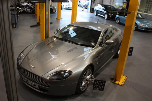 V8 Vantage tuning (SLINC) - TDI Inspection Service - Page 1 - Aston Martin - PistonHeads - The image captures a spacious indoor garage, where a modern gray Aston Martin DB9 sports car is parked. The garage lighting illuminates the car's sleek design and shiny exterior, reflecting off the polished floor beneath. The registration plate '550 LNE' is visible, hinting at ownership. In the background, several other cars are parked, suggesting the garage stores more high-end vehicles, ready to be showcased or displayed to potential buyers.