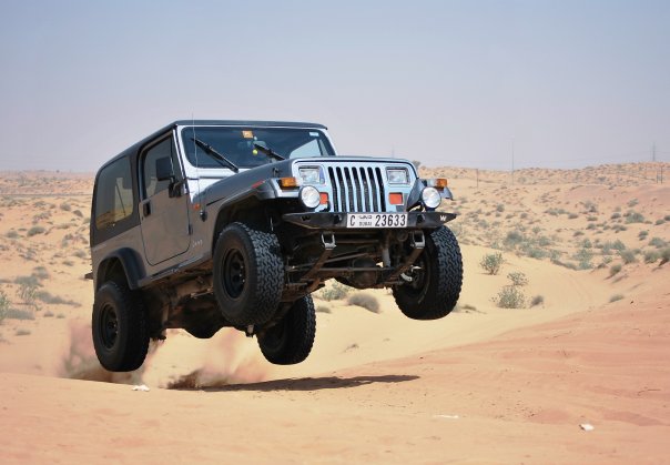 Pistonheads - The image captures a moment of excitement and action, featuring a black four-wheel-drive SUV having lost contact with the ground on a sandy dune amidst a vast desert landscape. The vehicle is airborne, hovering slightly above the dune, showcasing a sensation of speed and power. The license plate of the SUV sits prominently in the center, reading "C2533," adding a personal touch to the scene. In the background, the horizon line can be seen, further enhancing the expansive feel of the desert environment.