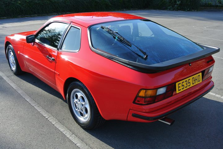 944/968   Post your pics. - Page 1 - Front Engined Porsches - PistonHeads - The image depicts a red Porsche 911 from the year 1986, parked on a tarmac lot. The car's hood is angled for better ventilation. On the right side of the vehicle, a pair of curved antennas extends outward. The license plate is clearly visible and reads "E53 OHD." The overall condition of the car suggests it is well-maintained.