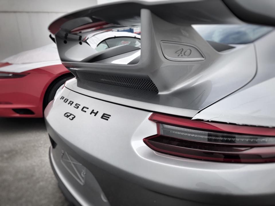 991.2 GT3 - Colours. Spec. Q+A. etc etc.. - Page 63 - 911/Carrera GT - PistonHeads - The image depicts a rear view of a silver Porsche sports car. Its tail end is painted a sleek silver, highlighted by a red stripe that matches the taillights. Just above the red stripe, the Porsche logo is prominently displayed, indicating the brand of the vehicle. The backdrop is an outdoor setting with another car in the background, possibly parked at a dealership or a car show. The overall composition emphasizes the elegance and power associated with luxury and sports car brands.