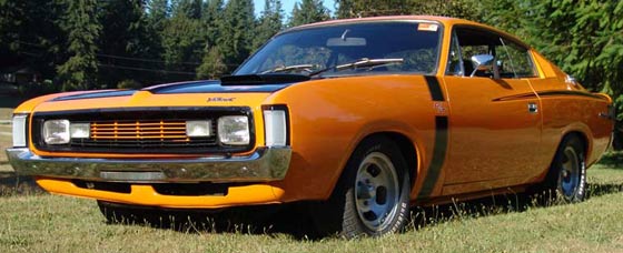 Americanaustralian Pistonheads - The image showcases an orange vintage car parked in a grassy area. The vehicle is an old Model T, distinguishable by its dual headlights and round hubcaps. The car is stationary, possibly in a wooded environment given the trees in the background, and appears to be the only vehicle in the immediate vicinity. The vivid orange of the car contrasts with the natural surroundings, drawing attention to its classic design.