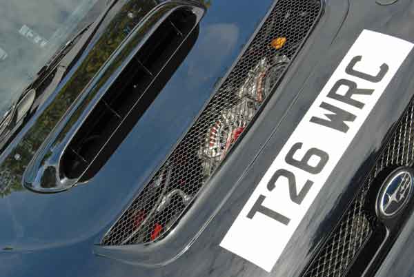 A close up of a street sign with a sky background - Pistonheads - The image showcases a close-up view of the front-right side of a vehicle, featuring a license plate with the characters "R26". Positioned just below the license plate, a grille with a mesh pattern is clearly visible, and within it, the brand 'TOYOTA' is discernible. The grille and license plate are set against the backdrop of a dark blue or black car, which occupies most of the image. The front of the vehicle is well-lit, indicating the photo was taken during the day.