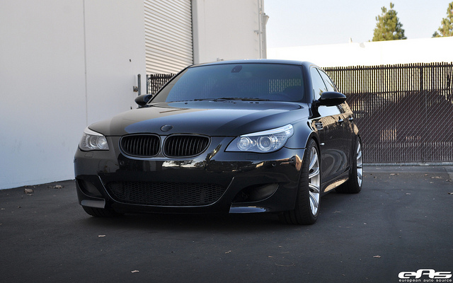 A car parked on the side of the road - Pistonheads - The image shows a modern black BMW car parked on a concrete surface. The car is facing towards the right side of the image, and its front grille features the distinctive emblem of the BMW brand. The vehicle appears to be in good condition and is positioned against a backdrop of a white building and a chain-link fence. The lighting in the photograph is even, suggesting it might be a clear day. There's a watermark in the lower right corner that reads "aumopark," indicating that this might be the name of the automobile photography studio or service.