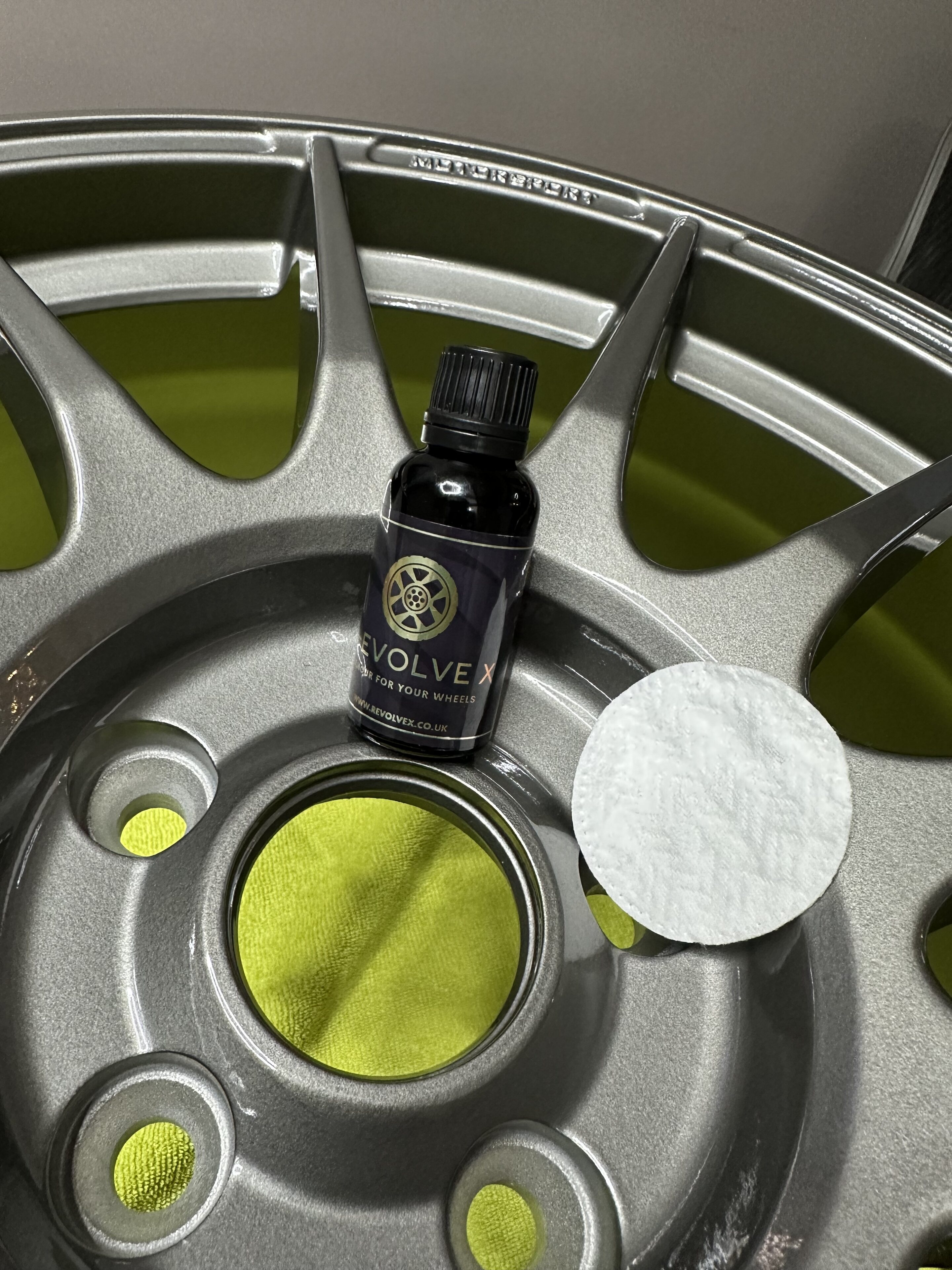 Pistonheads - The image presents a scene involving car wheels and a bottle of oil. In the foreground, there is a single silver car wheel with a visible yellow sticker on its center hub. On top of this wheel, there is a small dark-colored bottle, which appears to be an oil for wheels or a similar automotive product. The label on the bottle is facing upwards and seems to contain text, although it's not clearly legible in the image.

The wheel is placed inside a circular object that resembles a car rim, with visible silver spokes suggesting its design. This object has a black background, which provides a stark contrast to the wheel and bottle. The overall setting of this image seems to be a garage or workshop, as indicated by the presence of what appears to be a workbench in the background.

The image is taken from an elevated angle, looking down upon the wheel and bottle, which gives a clear view of their details. The lighting in the scene casts soft shadows around the wheel, indicating that the light source is coming from above and at an angle. This creates a sense of depth in the image, with the light creating subtle highlights on the car wheel and the oil bottle.