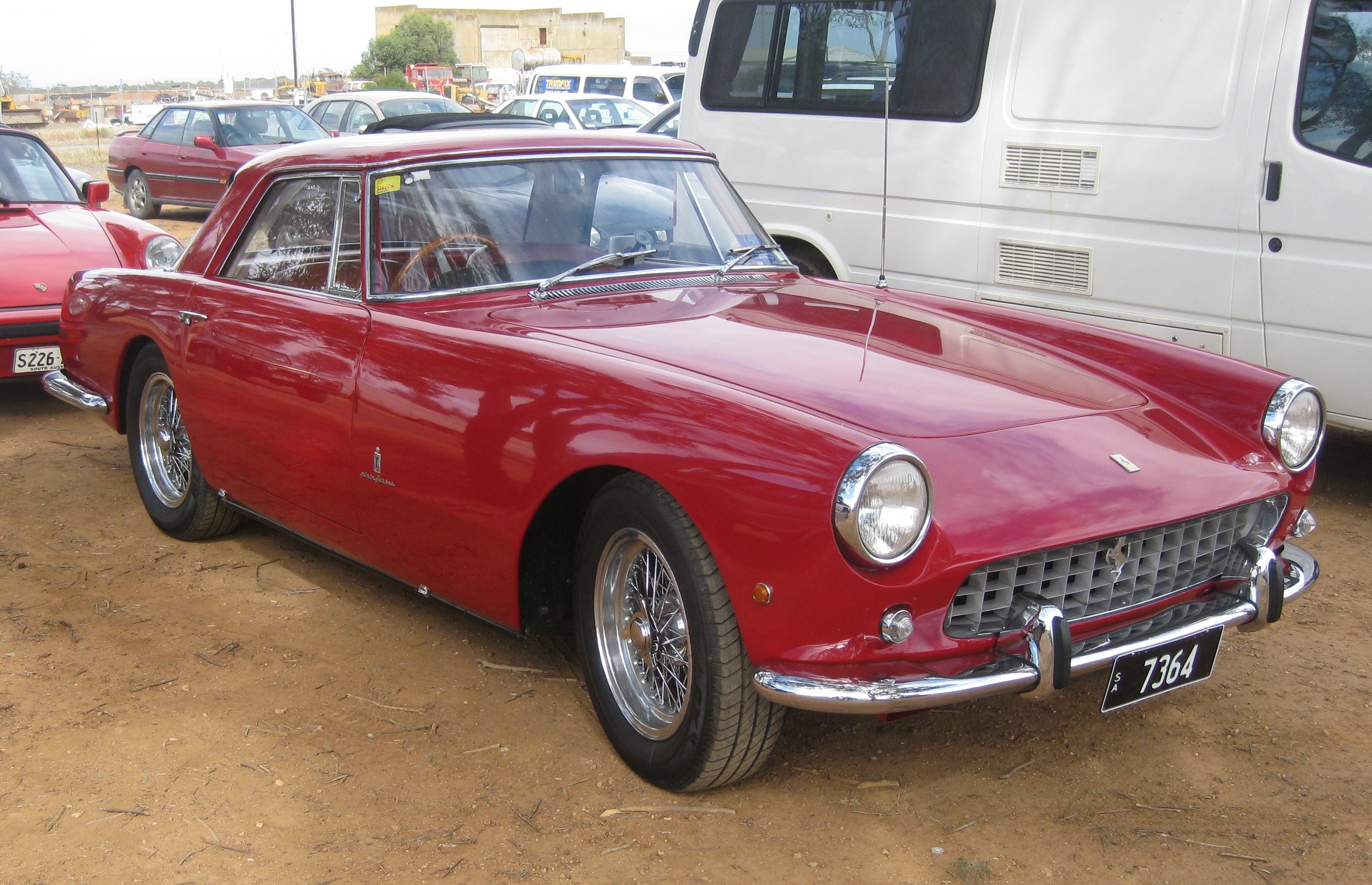 Classic (old, retro) cars for sale £0-5k - Page 384 - General Gassing - PistonHeads - The image features a vintage two-door car, painted in a striking shade of red. The car, which has round taillights, is parked on a dirt surface in an outdoor lot where other vehicles are also present. The car's design suggests it's older, likely from the mid-20th century, and it remains in good condition. The license plate is visible and accompanied by a number that is similar to that of the traditional driver's permit numbers often seen in car shows or club gatherings.