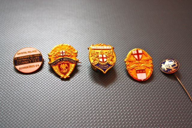 Have these got any value/history? - Page 1 - Sports - PistonHeads - The image displays a collection of five vintage enamel badges neatly arranged in a row on a dark gray background. From left to right, the badges feature emblems and text designating them as part of the Crystal Palace Miniature Committee of the Great Exhibition London 1924, an organization associated with Crystal Palace. The style and condition of the badges suggest they are of antique or vintage origin. In the bottom right corner of the image, there's a small, narrow pin that appears to be a brooch or lapel pin, adding contrast to the collection of larger badges.