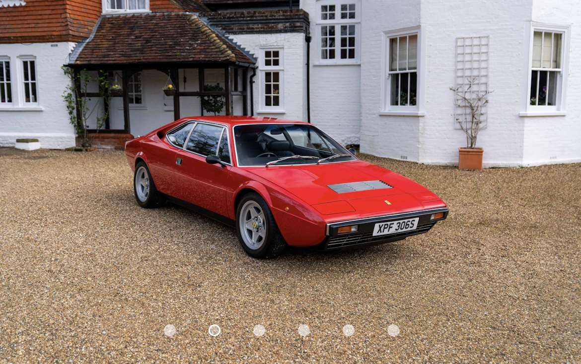 Pistonheads - The image displays a classic, red sports car parked on a gravel driveway in front of a house. The car is positioned at an angle to the camera, showcasing its side profile. It has a distinctive aerodynamic design with a large rear wing and a front spoiler, typical of high-performance vehicles from the 1970s or 1980s. The car is adorned with various graphics and designs on its body, indicating that it might be customized or used in racing events. There's a small amount of text visible in the image, but it's not clearly legible. The setting suggests that this could be a private residence, given the residential style house in the background.