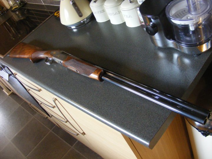 The PH Gun Cabinet - Shooting Matters - Page 10 - Sports - PistonHeads - The image displays a long, wooden barrel shotgun sitting on a gray kitchen countertop. The barrel is bare, missing its stock, but the trigger and forestock are still attached. Behind the shotgun, different kitchen items can be seen, including a toaster, a few cans, and a mixer. The setting suggests a domestic environment, but the presence of the shotgun is unexpected and somewhat incongruous.