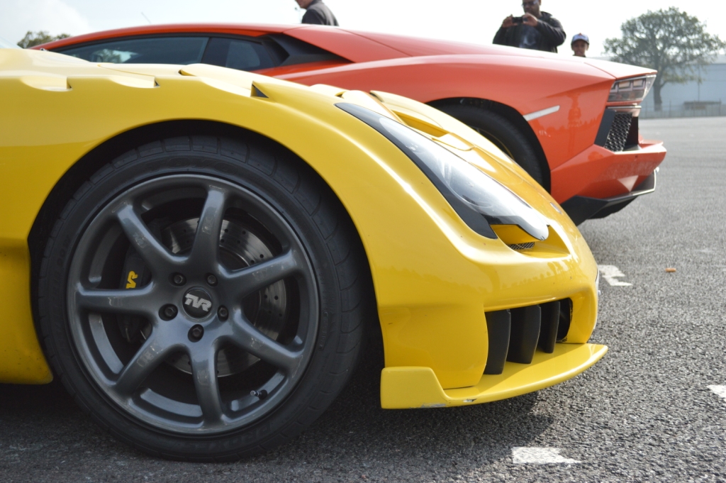 RE: Ferrari Racing Days Sunday Service 14/09 - Page 10 - Sunday Service - PistonHeads - This image displays two luxury sports cars positioned side by side, likely in an outdoor setting, with a person in the background on the left. The car closer to the left side of the frame is predominantly yellow, while the one on the right is predominantly red. Both cars feature aerodynamic designs, and at least part of the yellow car's rear bumper is visible. The pavement on which the cars are parked has white markings, suggesting it's a designated parking or display area. The lighting in the photo indicates it might be daytime, given the shadows and the brightness in some areas.