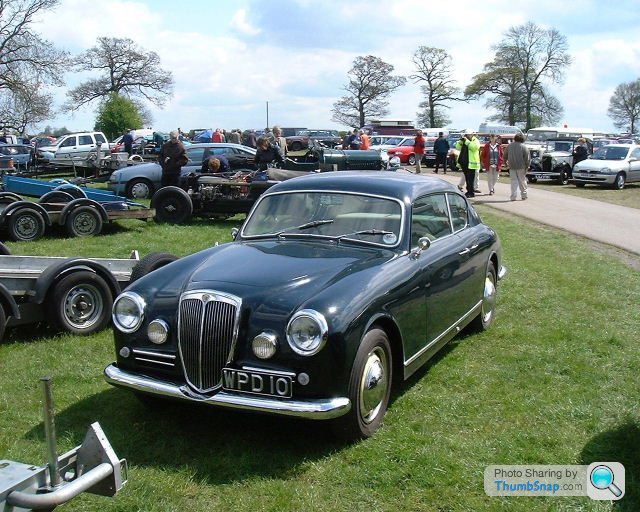 Dear Dtype Pistonheads - The image captures a vintage scene, highlighting a classic black car as its focal point. The black car is parked on grassy terrain, suggesting an open, outdoor event. In the background, an array of vehicles, including antique trucks and cars, are on display, indicating a celebration or exhibition of vintage vehicles. The presence of a crowd of people, visible on the upper right side of the image, further suggests a public event, where enthusiasts have gathered to appreciate the classic vehicles.