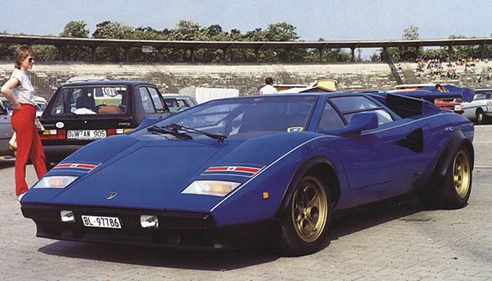 Countach  - Page 12 - Lamborghini Classics - PistonHeads - The image showcases a vibrant blue sports car, which is the center of attention, parked on a crowded street. The car's striking blue color contrasts with the grey tones of the road and the slightly blurred image of an old stadium in the background. Several spectators are in the vicinity of the car, indicating a possible special event or exhibition. The perspective of the photo gives a sense of the grandeur of the vehicle, placed prominently in front of the spectators and the stadium.