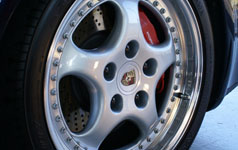 Better than a Speedline ? - Page 1 - Porsche Classics - PistonHeads - The image features a close-up of a silver car wheel. The wheel is fitted with a unique design that includes black bolts and red-branded inserts. Each spoke on the wheel has a series of smaller bolts, adding to the intricate design of the wheel. The background is not clear, but it appears to be a hard, flat surface, suggesting the close-up shot might have been taken from under the car.