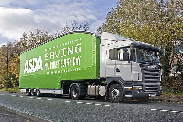 So, what exactly do you do then? - Page 1 - Commercial Break - PistonHeads - The image shows a large, green truck with the word "SAVING" in white letters on its side, suggesting an advertising campaign. The truck is driving down a road, surrounded by trees and bushes that provide a shaded environment. The sky is partly cloudy, indicating favorable weather conditions. The truck's front end and most of its side are clearly visible, showcasing its size and color scheme.