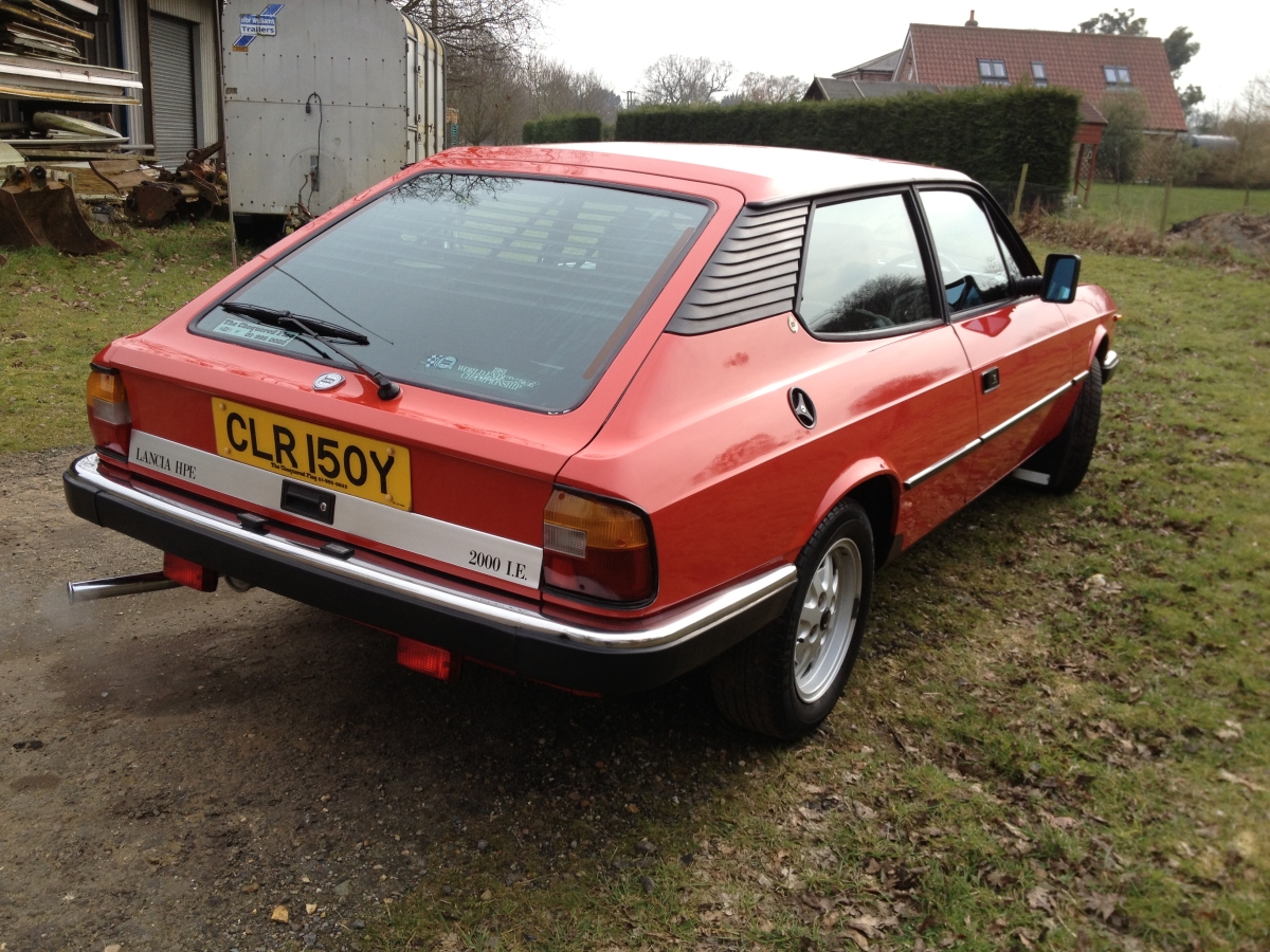 Lets see your Lancia's! - Page 25 - Alfa Romeo, Fiat & Lancia - PistonHeads - This image features an orange-red car parked on a grassy area. The vehicle has a registration plate that reads "CLR150Y." The side of the car is yellow, and the back is red. The car is positioned next to a building, and there is a smaller structure with metal siding visible in the background. The photo seems to be taken in an outdoor or dirt track setting.