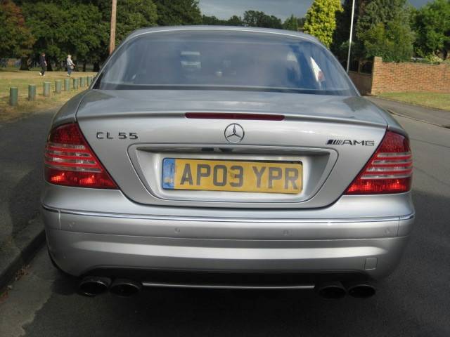 Pistonheads - The image captures a gray Mercedes-Benz CLS55 car parked on the side of the road. The car's registration plate is clearly visible, displaying the letters "AP03 YPR". In addition to the license plate, other distinguishing features include a Mercedes-Benz logo on the grille and a distinct side badge. The vehicle has four exhaust pipes, two on each side, adding to its distinctive look. The surrounding environment suggests this scene takes place in a suburban or residential area with greenery and a brick wall visible in the background.