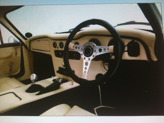 Early TVR Pictures - Page 101 - Classics - PistonHeads - The image presents the interior of a sports car, focusing on the dashboard and steering wheel. The steering wheel is positioned in the center of the image, exhibitinng a black and silver design with three silver buttons on the left. To the right of the wheel, high-quality speakers are visible, likely part of a premium audio system. The dashboard is dominated by a white and yellow color scheme, while the seats are upholstered in a cream fabric, adding to the luxury of the vehicle. Lastly, there is a small silver shift knob on the left side of the image, indicating the car's manual transmission.