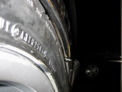 The image presents a close-up view of a vehicle's hubcap. The hubcap is black and is etched with various texts and numbers, indicating it is likely an early Ford Ranger or a similar model. Interestingly, there appears to be a yellowed paper underneath the hubcap, which may suggest that the vehicle's owner is a smoker, as the interior of the car might be yellowed due to smoking. The interior part of the hubcap also shows some scratches and signs of wear, which is common for wheel rims. The rest of the vehicle's interior is shrouded in darkness, emphasizing the focus on the hubcap.