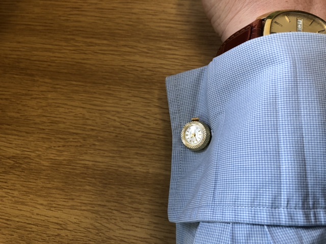 Wrist Check - 2019 - Page 127 - Watches - PistonHeads - The image captures a person's wrist, adorned with a gold watch. A button-up shirt is cuffed at the sleeves, revealing a pattern of blue and white plaid. On top of this cuff, a blue pocket square peeks out, adding a touch of color to the ensemble. The background is blurred, drawing focus to the wristwatch and the details of the shirt.