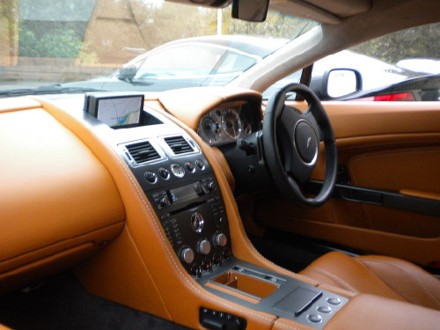 Interior Kestrel Pistonheads - The image portrays an interior view from the perspective of a passenger in a luxurious vehicle. The car has a tan-colored interior with visible white stitching along the seams of the leather seats. The front seat is fully visible, showcasing the driver's side. On the center console, there's a variety of controls and possibly a screen, indicative of the car's advanced technological features. The sun visor is lowered, and the car appears to be in a parked position, with another vehicle visible through the side windows.