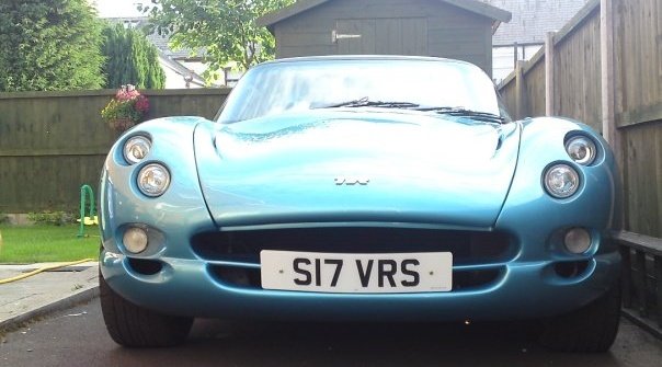 Headlight Pistonheads Conversion - The image shows a silver or blue-colored classic sports car. The vehicle is parked on a driveway and occupies a significant portion of the frame. The design of the car has a striking presence, with a blend of curves and angular lines that give it a distinctive appearance. The setting appears to be a residential driveway with a house visible in the background. The car's license plate is clearly visible and reading "S17 VRS". The overall style of the image is a standard photograph without any filters or alterations.
