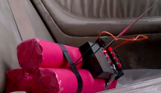 Great Tracker tag solution..... - Page 1 - Aston Martin - PistonHeads - The image displays a homemade explosive device seated on a car seat. The device appears to be a low-explosive device, likely a small-scale improvised explosive using pink plastic as casings, red electronics, black fuses, and green wires. Multiple electronic components are visible on the device, suggesting it has been wired to potentially ignite the explosive material inside the casings. The image has a dim lighting condition, which may be intended to obscure sensitive components or to imitate a low-light surveillance setting. The design and construction of the device strongly indicate that it is a non-professional creation, possibly for entertainment or educational purposes with no intended purpose for real-world explosive situations.