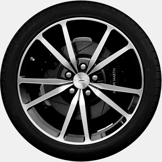 Anyone run 20 inch alloys on a Vantage - Page 1 - Aston Martin - PistonHeads - The image is a close-up photograph of a car wheel. It features alloy rims and the central metal hub. The spokes of the wheel are silver and display a polished metallic finish. The outer edge of the wheel has a black rubber trim, and there is text visible, which appears to be the name "Martin" on the hub and "I.B De Nemiert" in a triangular area on the side of the rim. The photo has a clear focus on the wheel, creating a slightly distorted background due to the close shot.