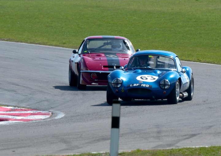 Pictures of your racecar thread - Page 1 - UK Club Motorsport - PistonHeads - The image captures a thrilling scene on a race track, where two vintage cars are in the midst of a race. The leading car is a distinctive combination of blue and white, bearing the number 63. Just a car length behind lies a mid-red themed car, following the leader's line tight. Both cars are leaning sideways as they round a sharp bend in the track, their polished bodies reflecting the intensity of the race. The grassy surroundings and the cloudy sky in the background frame the exciting action on the track.