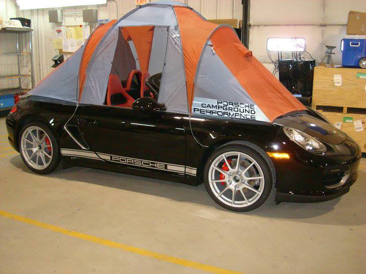 Le Mans special Boxster Spyder - Page 1 - Boxster/Cayman - PistonHeads - This image features an unusual sight: a black Porsche Cayman sports car has been converted into a makeshift tent filled with sleeping bags. The tent is pitched over the entire body of the car, spanning from the front to the back. Inside the car, you can see the outline of the vehicle's seats, but the details are obscured by the thick fabric of the tent. The overall scene is whimsical and eclectic, blending the luxury of a sportscar with the camping culture of tent life.