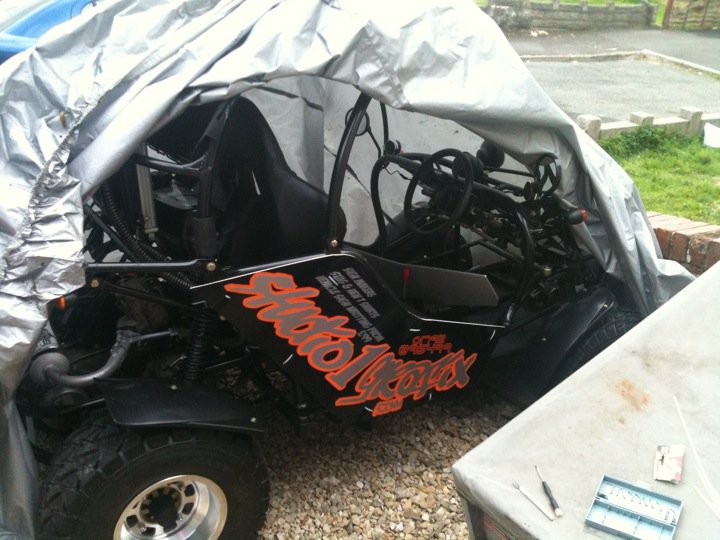 Open Byways Legal Traffic Pistonheads - The image shows a quad bike, also known as an all-terrain vehicle (ATV). One side of the ATV is covered with silver duct tape and plastic sheeting, while the other side is exposed. The letters "SR IS LOVES" are visible on the exposed side. The surrounding area seems to be an outdoor space with a grassy area nearby and a container with tools laid out near the ATV.