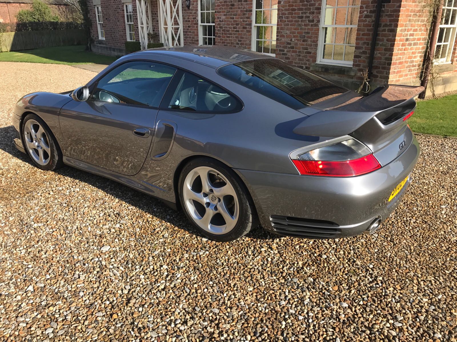 GT2 - Page 144 - Porsche General - PistonHeads - The image shows a gray Porsche parked on a gravel driveway in front of a building. The Porsche appears to be in good condition, with a sunroof and black side skirts. The tires have silver rims, and the car's paint reflects some of the surrounding light, indicating recent sunlight.