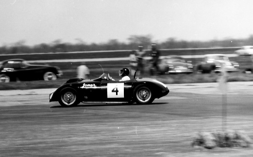 Early TVR Pictures - Page 33 - Classics - PistonHeads - This is a black and white photograph capturing a moment on a race track. The main focus of the image is a car numbered 4. The car is captured in mid-speed, suggesting movement and activity. In the background, there are five people watching from the sidelines. The track is lined with various types of vehicles, including cars and vintage sports cars. The image conveys a sense of excitement and anticipation, with the racing car and spectators making the scene dynamic and full of energy.