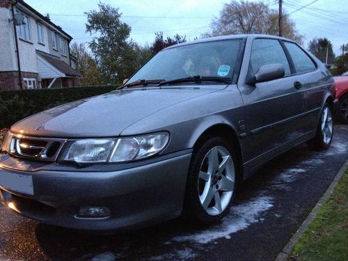 So I just bought a 9-3 Aero Hot....  - Page 1 - Saab - PistonHeads - The image displays a silver car parked on a street. The car is positioned diagonally in the frame, with its front left side visible to the viewer. It appears to be a compact model, possibly a hatchback, based on its shape and size. The vehicle has a shiny exterior and multiple air vents on the hood. The headlights of the car are turned off, and the license plate is clearly visible. In the background, there are some residential buildings, indicating a suburban or residential area. The lighting suggests it may be an evening or early morning setting.